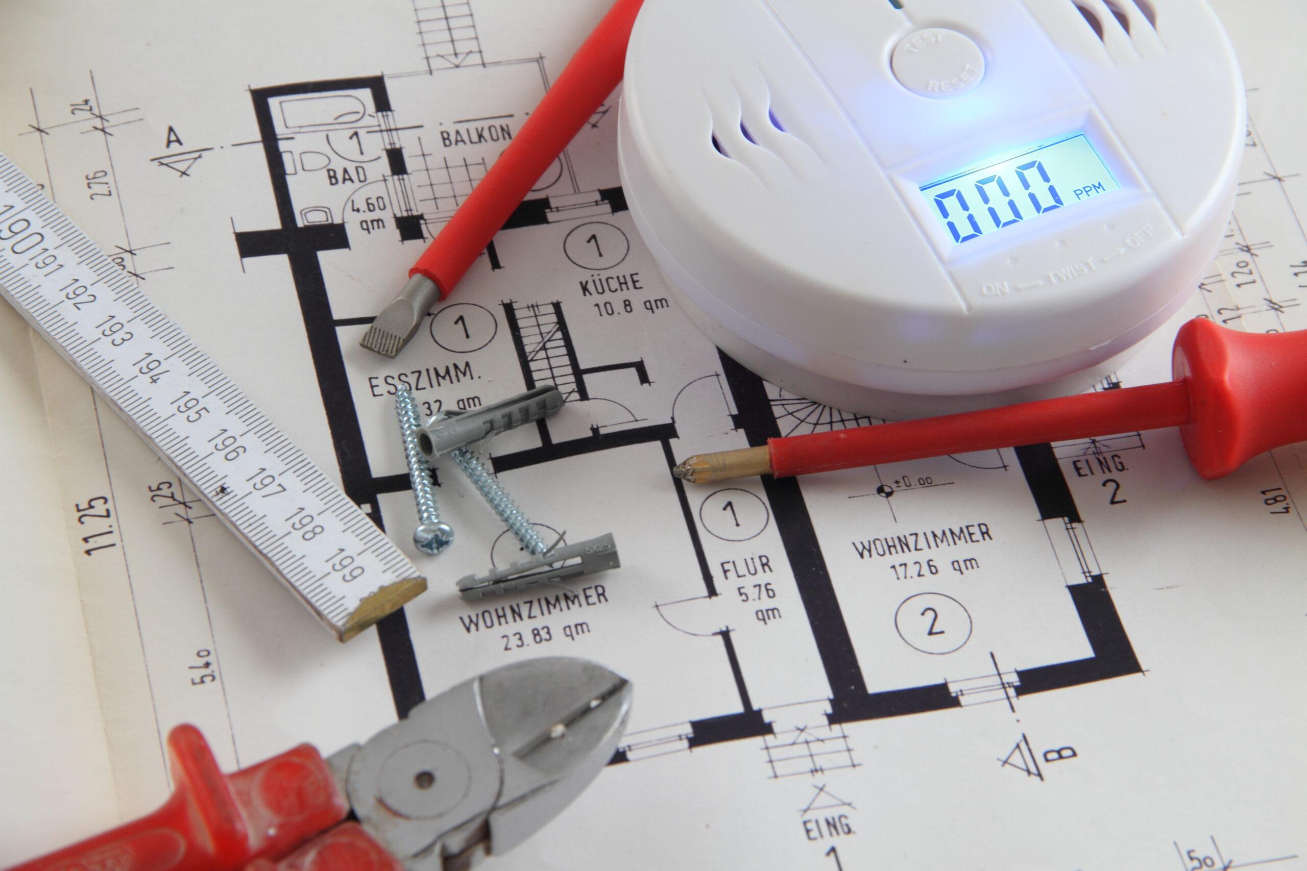 Bauplan mit Rauchmelder, Werkzeug und Schrauben auf Tisch | Brandwache Aufgaben